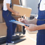 Delivery man checking list on clipboard near car